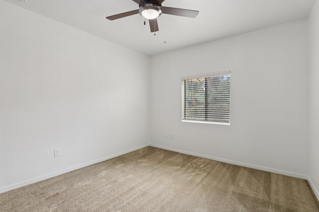A room with a ceiling fan and a window with blinds.