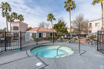 A hot tub sits in the middle of a patio surrounded by a black fence.