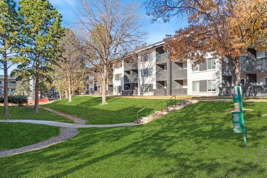 an apartment building with green grass and trees and a sidewalk