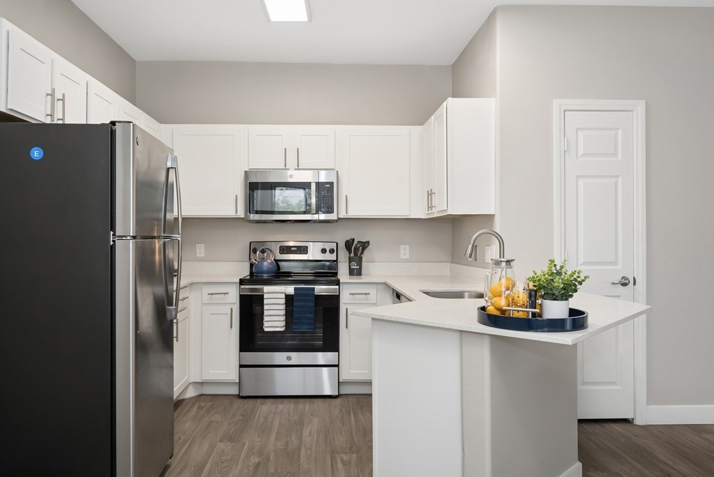 A kitchen with a black fridge, white cabinets, and a white island.