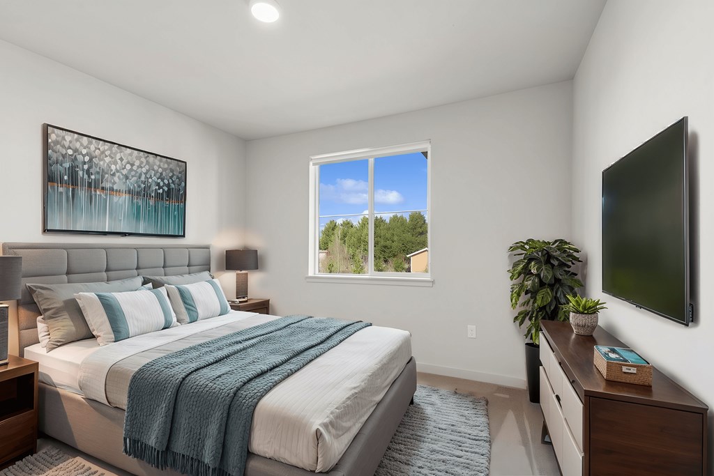 A bedroom with a large bed and a window showing trees outside.