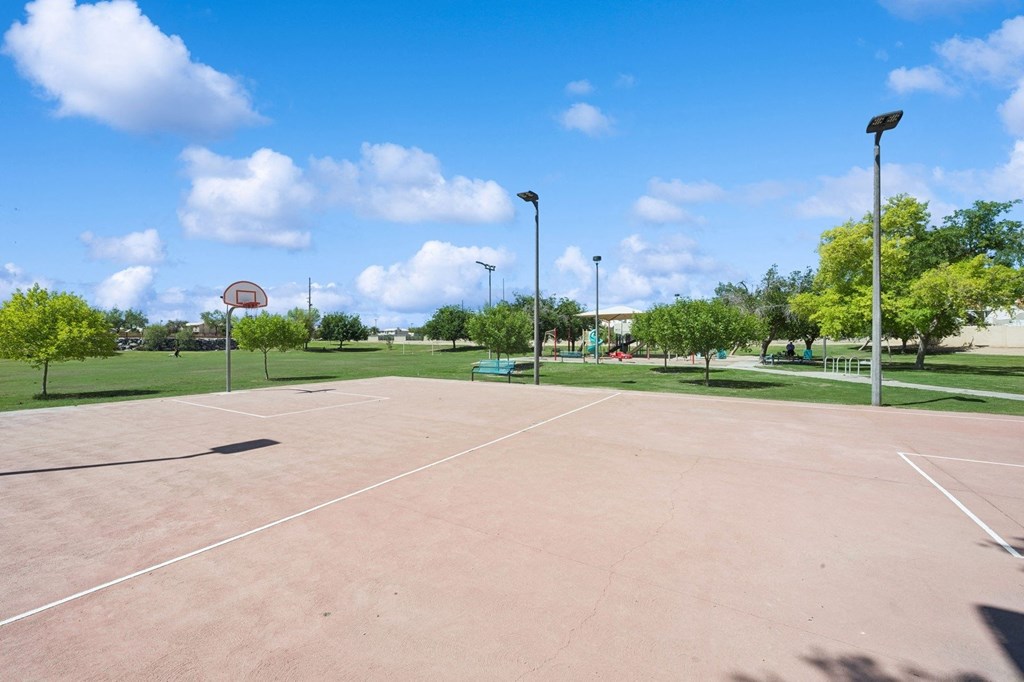 an empty basketball court in a park with trees