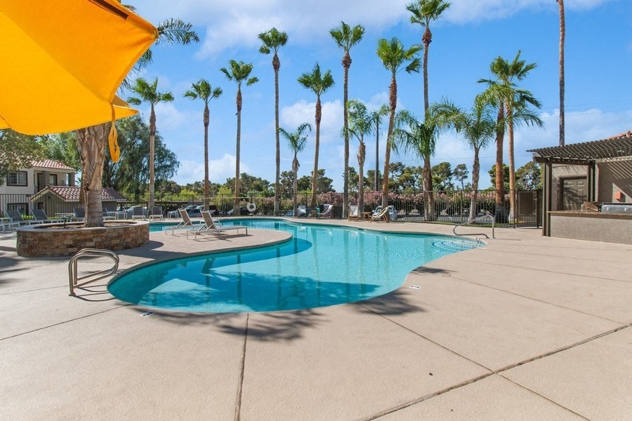 a swimming pool with a yellow umbrella and palm trees in the background