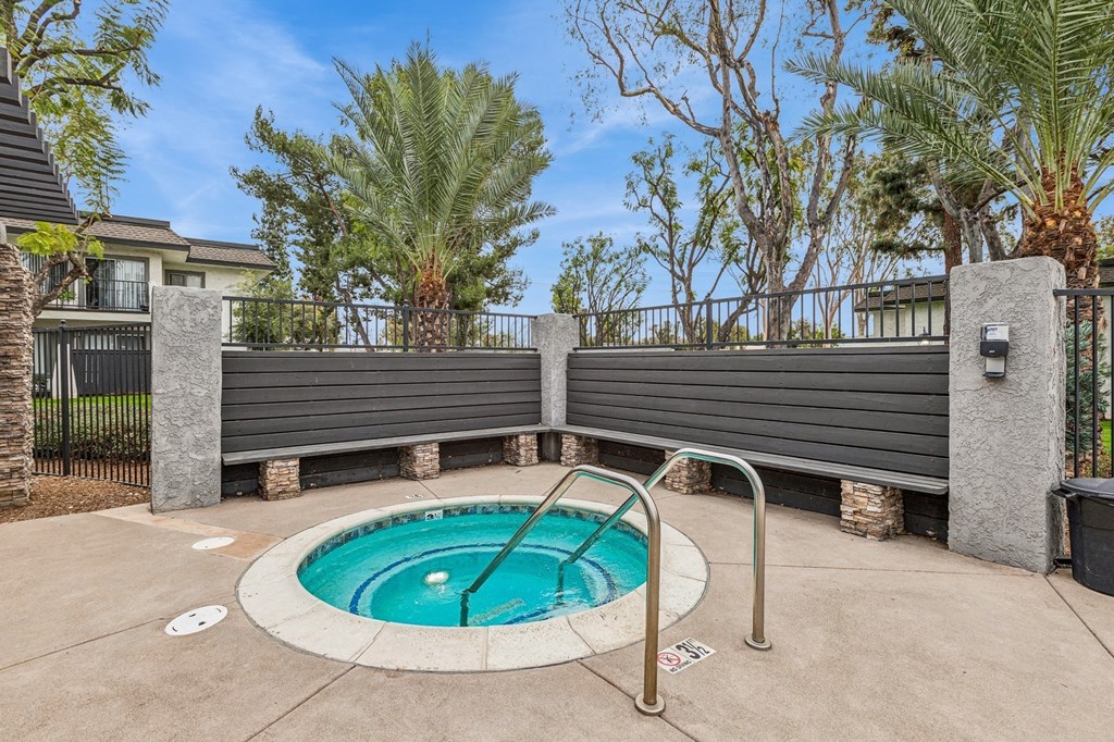 A small pool surrounded by a concrete patio and a metal fence.