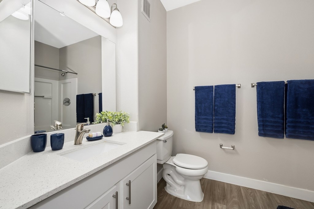 A white bathroom with a toilet, sink, and blue towels.