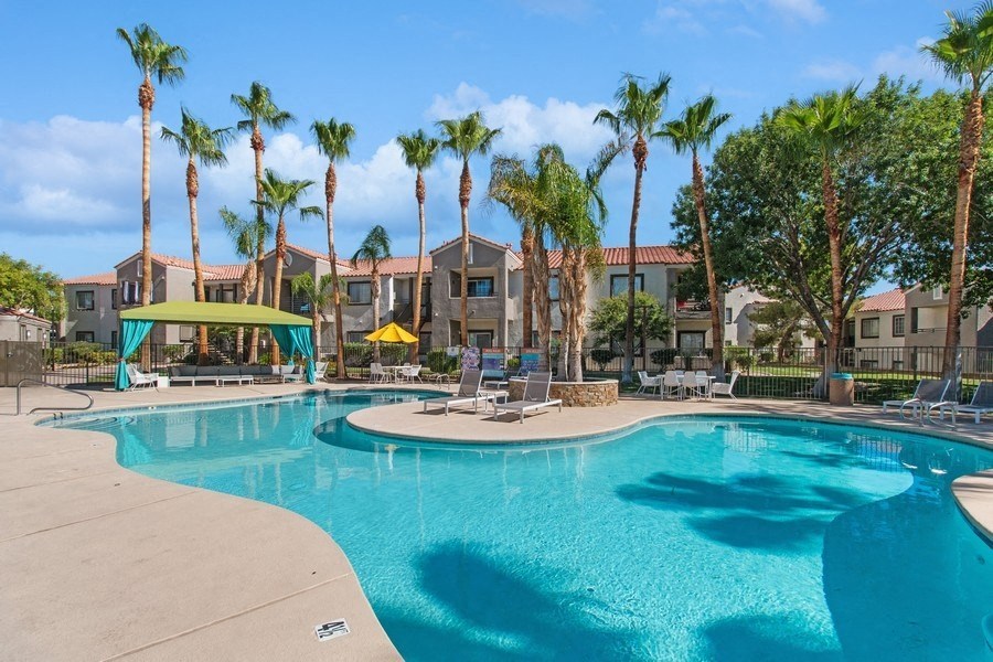 a resort style swimming pool with chaise lounge chairs and palm trees in the background