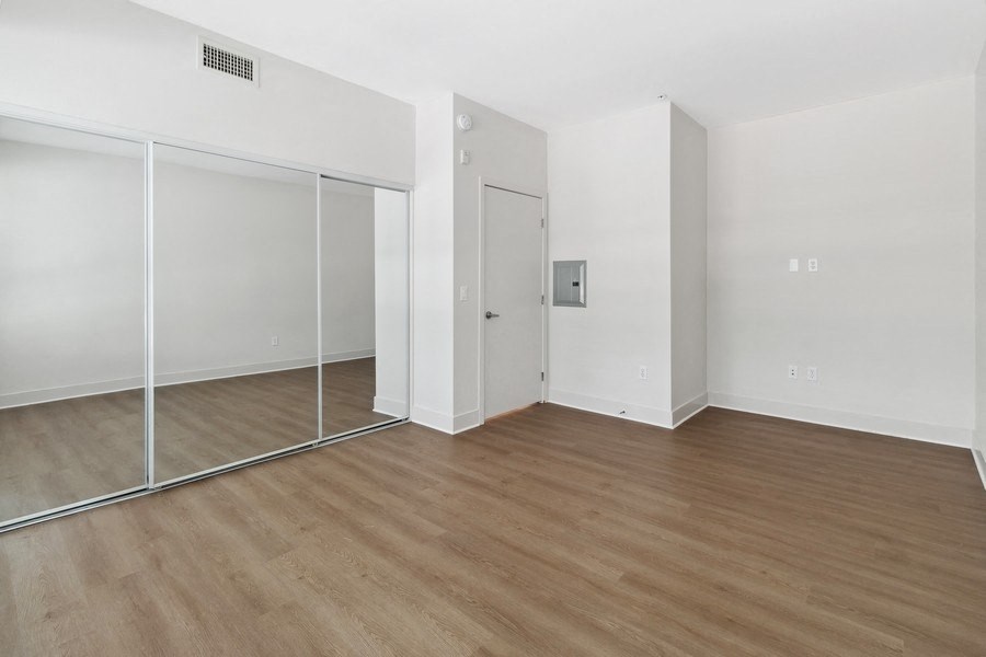 an empty room with white walls and wood flooring and a mirrored closet