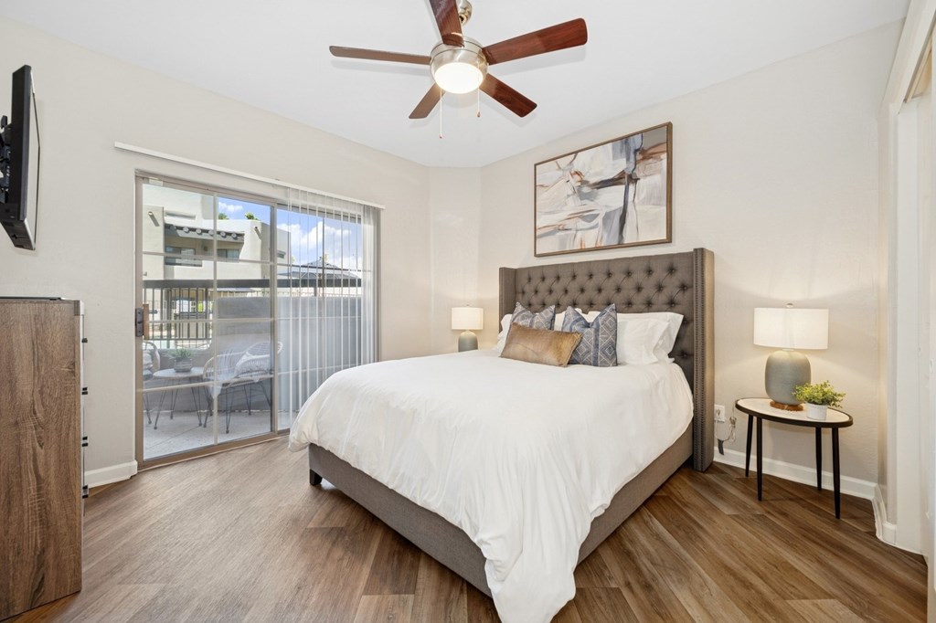 A bedroom with a bed, a ceiling fan, and a sliding glass door.
