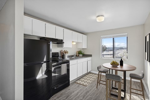 A black fridge and oven in a white kitchen with a table and chairs.