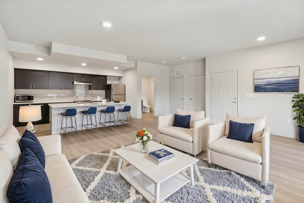 A modern living room with a white sofa, a coffee table, and a kitchen area in the background.