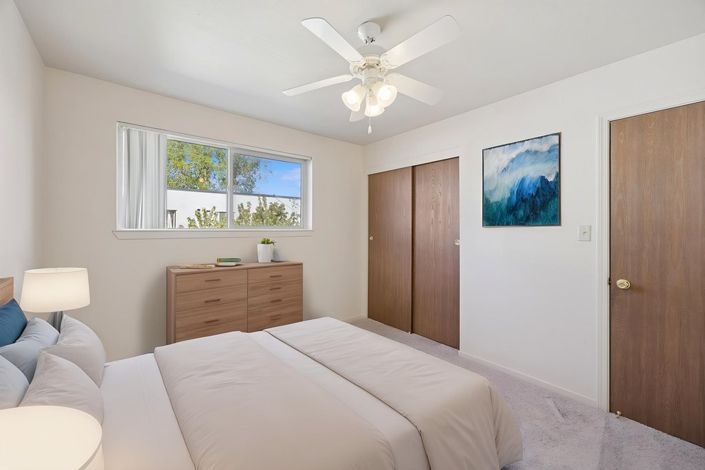 A bedroom with a large bed, a ceiling fan, and a painting on the wall.