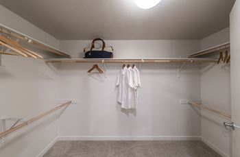 a walk in closet with a white wall and wooden shelves and a bag on top