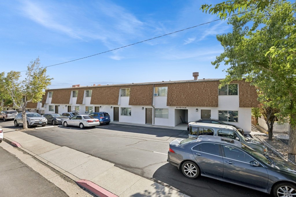 A street view of a residential area with cars parked on the side of the road and apartment buildings in the background.
