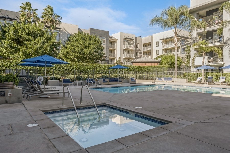 a swimming pool with chairs and umbrellas in front of an apartment building
