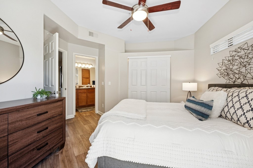 A bedroom with a large bed, a ceiling fan, and a wooden dresser.