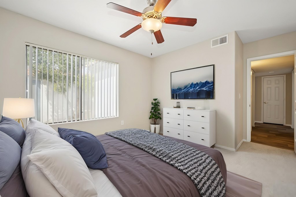 A bedroom with a bed, a ceiling fan, and a painting on the wall.
