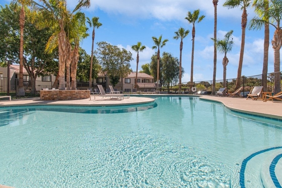 a resort style pool with chaise lounge chairs and palm trees in the background
