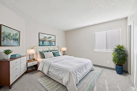 A bedroom with a large bed, a dresser, and a potted plant.