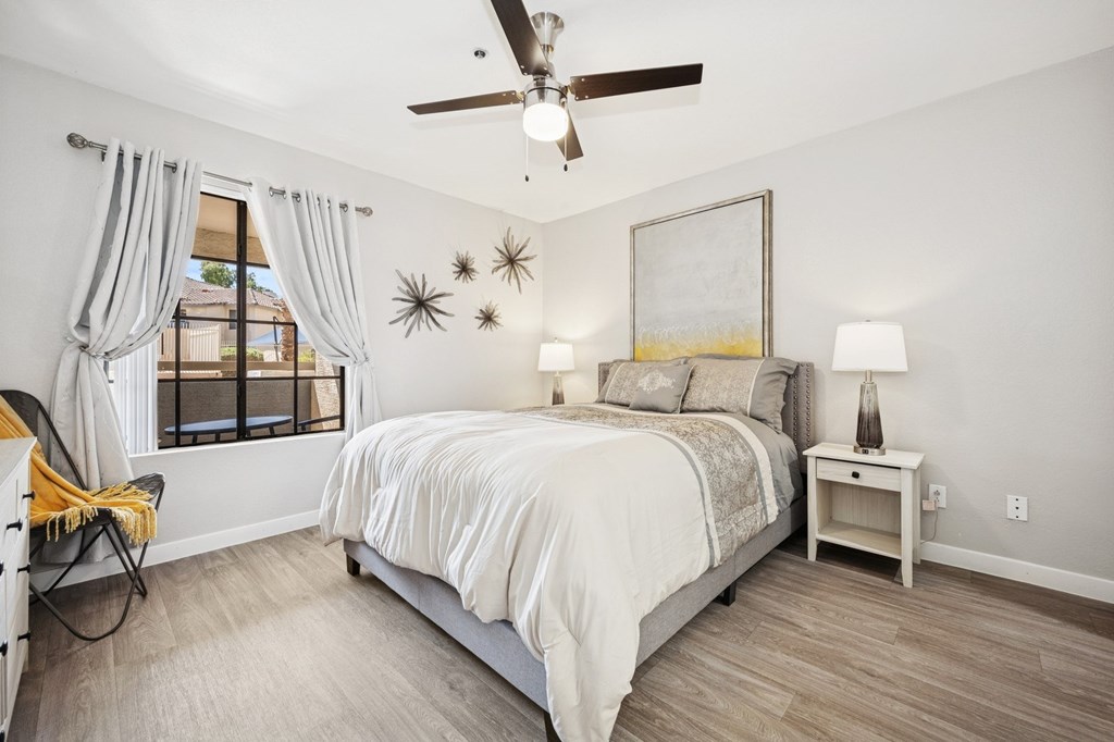 A bedroom with a bed, a chair, a ceiling fan, and a painting on the wall.