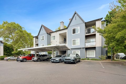 A grey apartment building with cars parked in front.