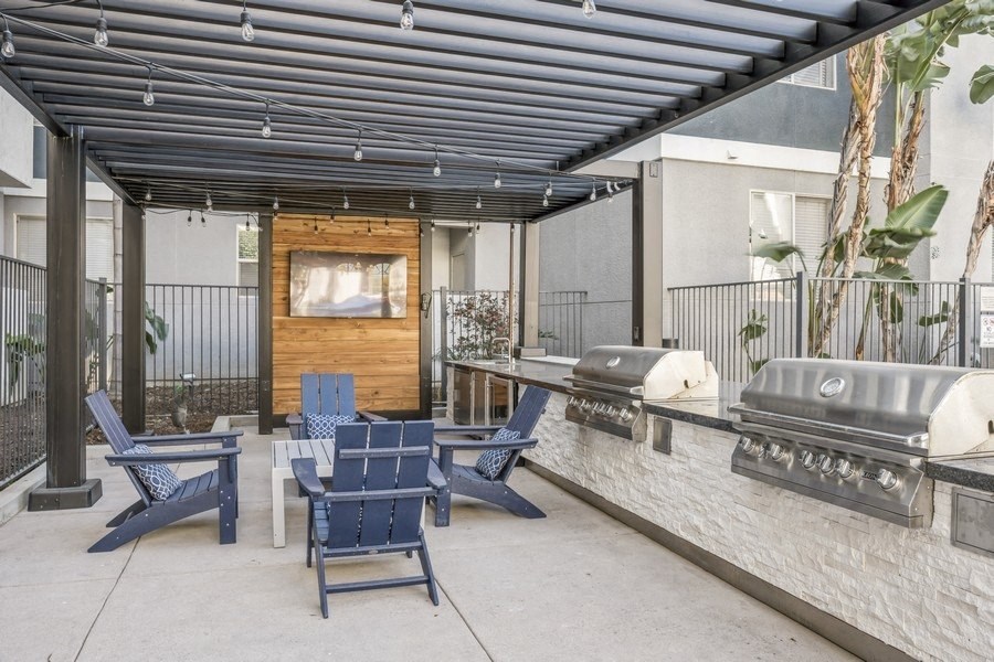 an outdoor patio with blue chairs and a grill and a tv