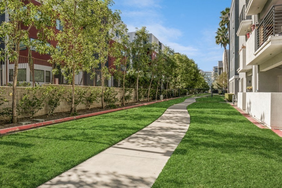 a walkway between two apartment buildings with green grass and trees