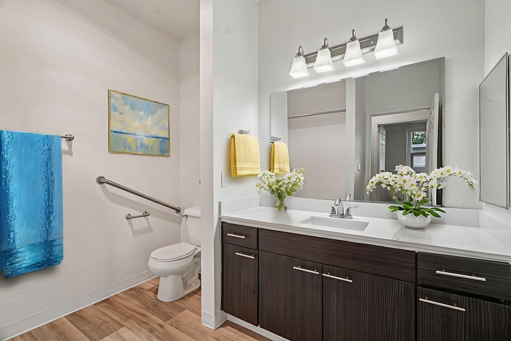 A bathroom with a blue towel and a painting of a sunny sky.