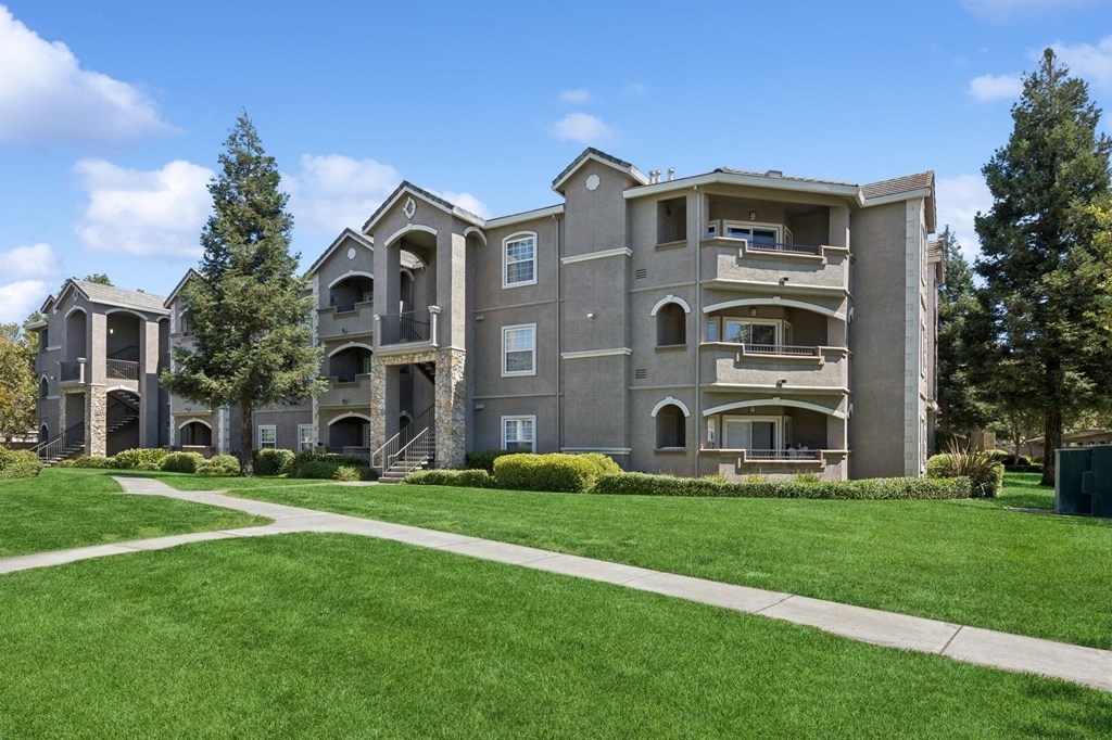 an apartment building with a green lawn and sidewalk
