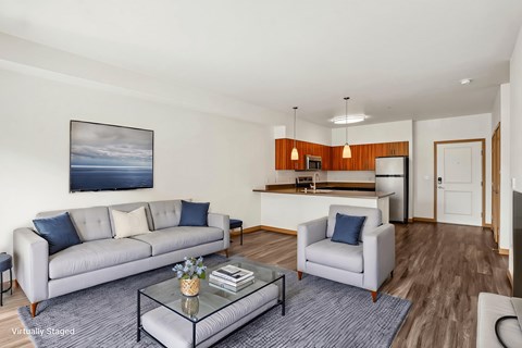 A living room with a grey couch, a glass coffee table, and a painting on the wall.