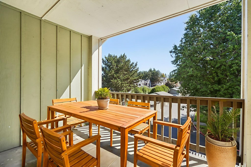 A wooden table and chairs on a balcony with a potted plant.