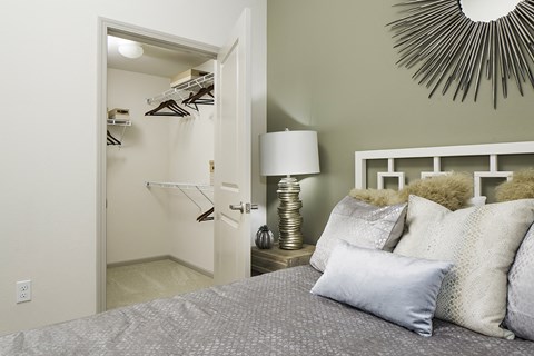 A bedroom with a bed, lamp, and a closet with clothes hanging.