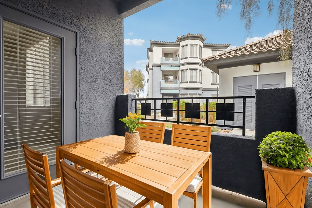 A wooden table with chairs and a vase of flowers on a balcony.