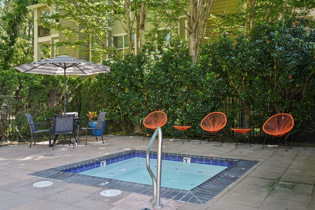 A pool surrounded by orange chairs and a green hedge.