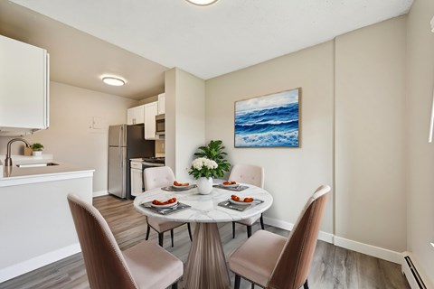 A dining room with a table set for two and a painting of the ocean on the wall.