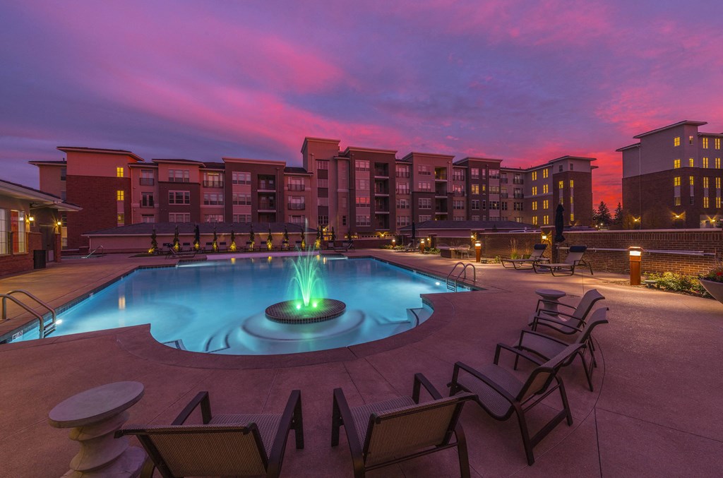 a pool with chairs and a fountain at night
