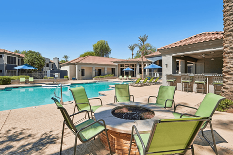 A poolside area with a fire pit and chairs.