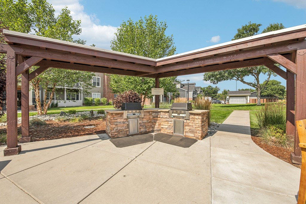 A wooden pergola over a concrete walkway with stone pillars.