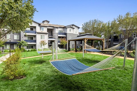 a yard with hammocks and a gazebo in front of an apartment