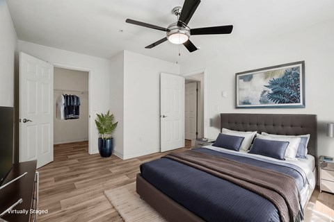 A bedroom with a bed, a ceiling fan, and a painting on the wall.