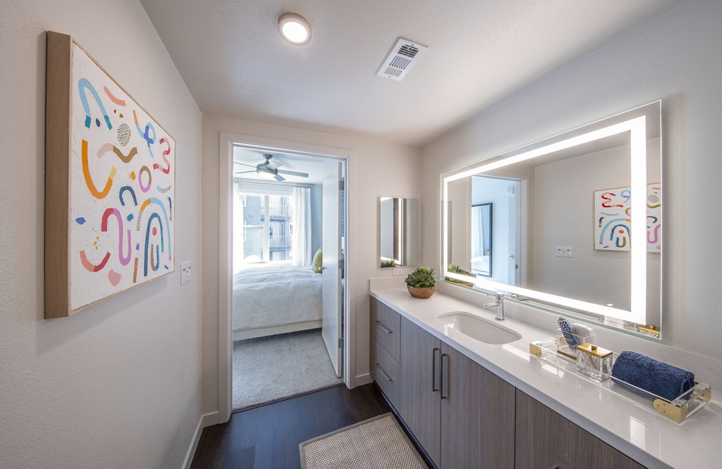 a bathroom with a sink and a mirror and a door to a bedroom