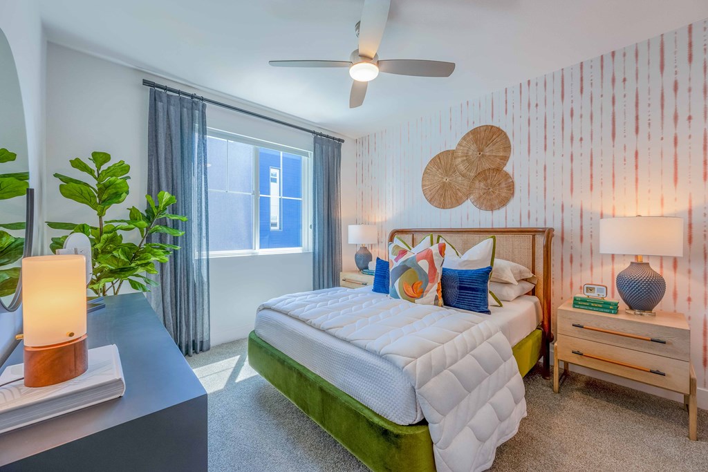 A bedroom with a bed, nightstand, and a plant.