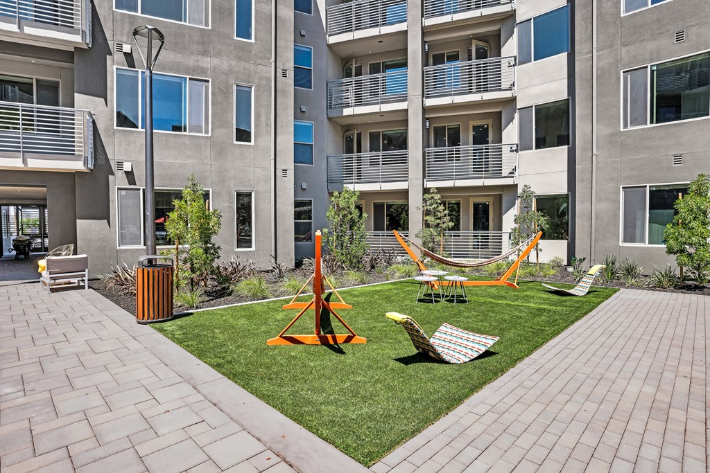 an apartment yard with hammocks and chairs in front of an apartment building