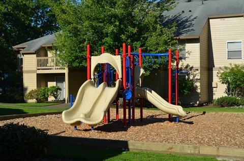 A playground with a yellow slide and red and blue poles.