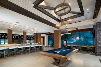A pool table is in the middle of a room with a bar and chairs.