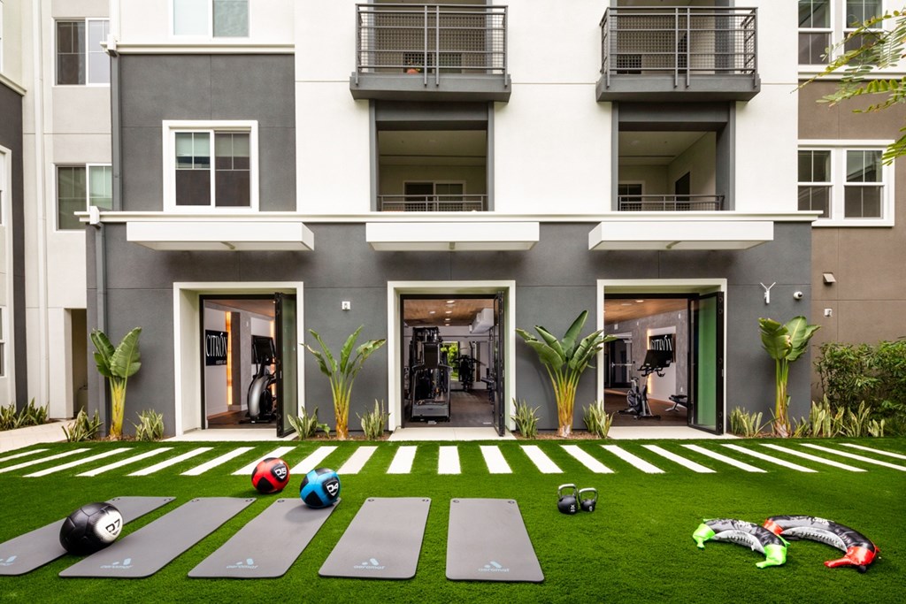 A yoga mat and exercise equipment are placed on a green lawn in front of a building.