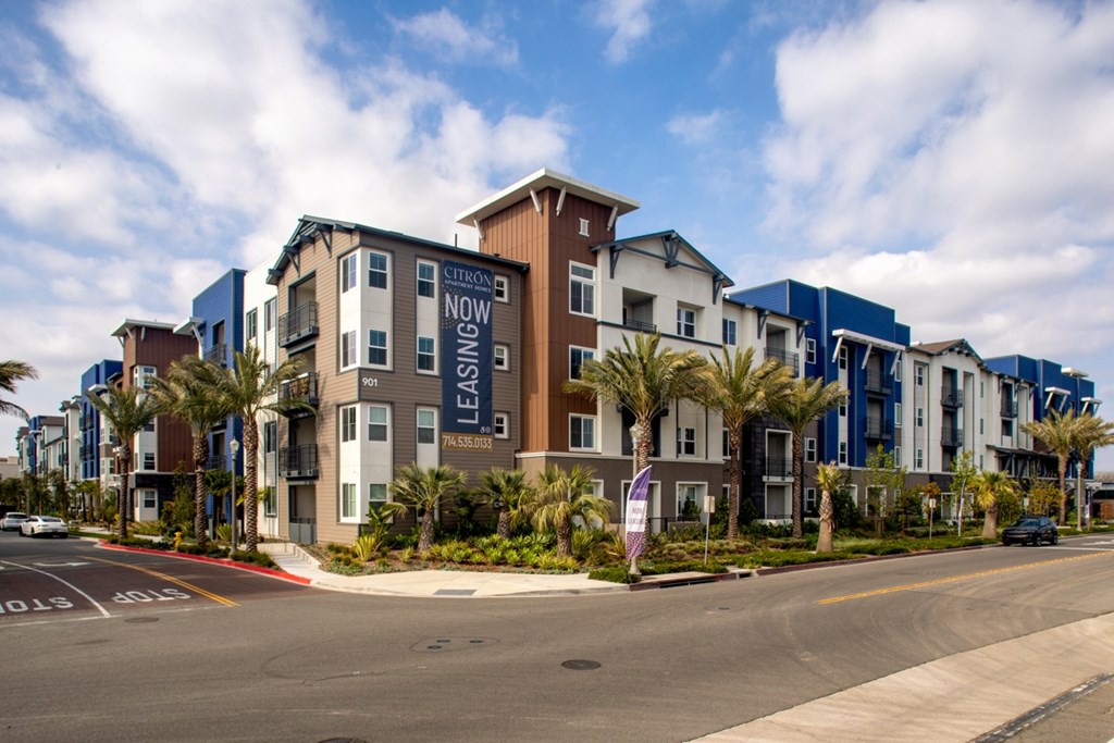 A street view of a residential area with apartment buildings and palm trees.
