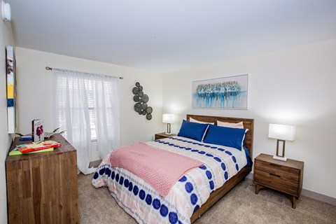 A bedroom with a bed, nightstand, and a painting on the wall.