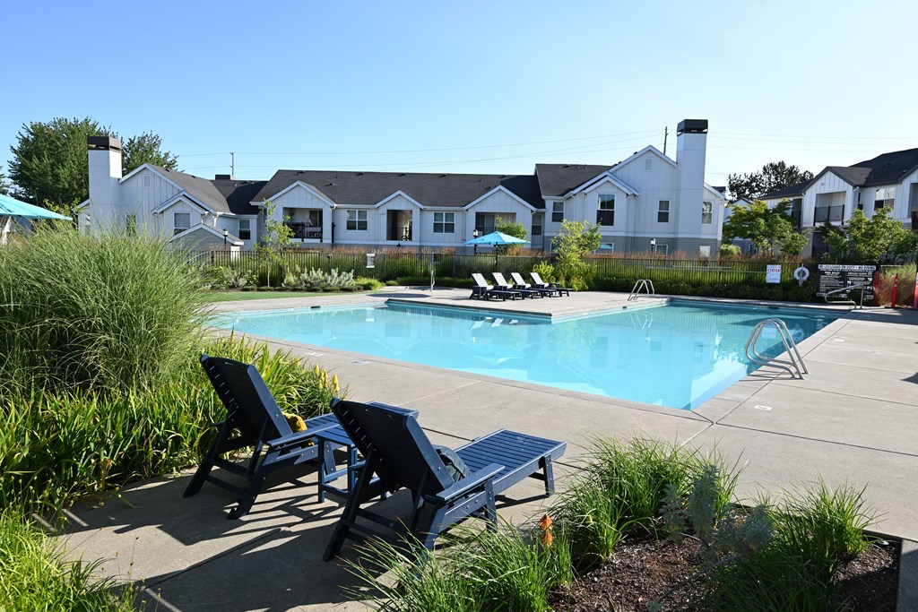A pool surrounded by chairs and a grassy area.