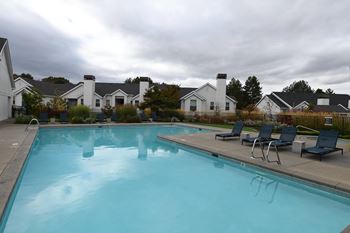 the view of a large swimming pool with chairs and houses in the background