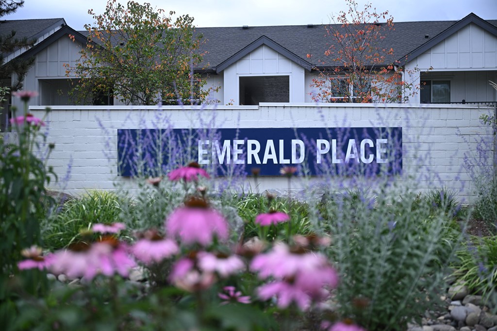 a sign for emerald place in front of a building with flowers